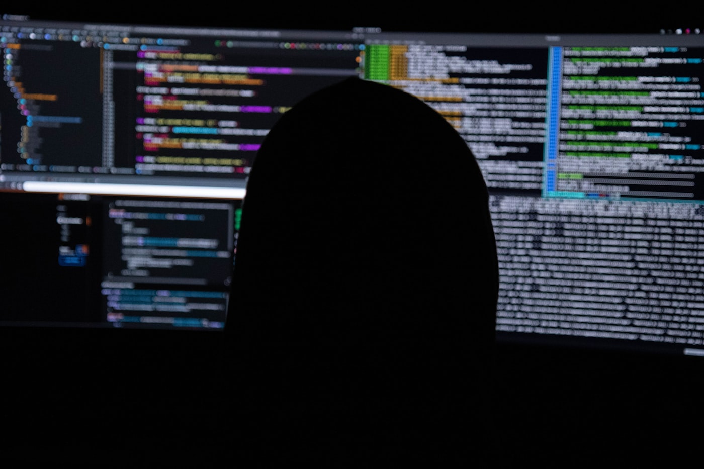 เงาบุคคลหน้าจอโค้ดหลายจอในห้องมืด สื่อถึงการโจมตี ransomware ที่ต้องเตรียมระบบกู้คืนข้อมูลไว้ล่วงหน้า
